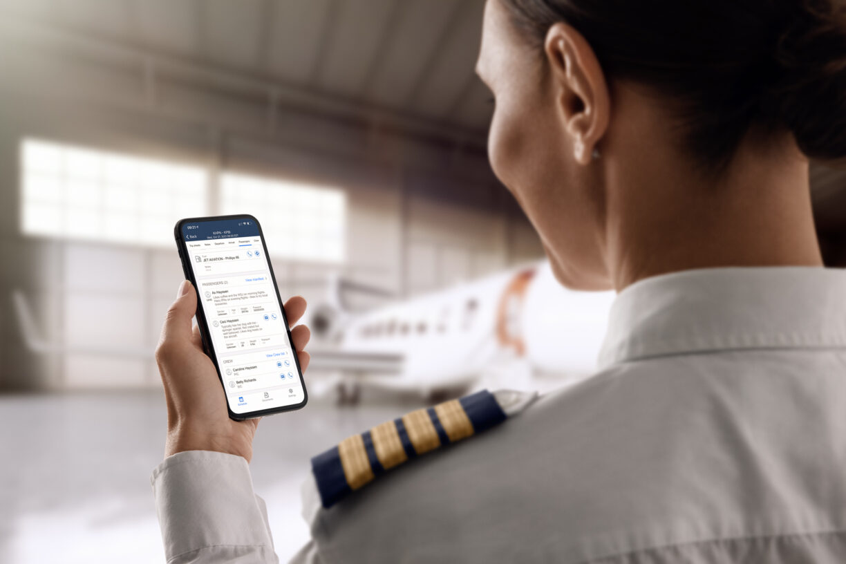 Image of a pilot taken from behind holding up her phone with the crew app, a jet is in the blurry background