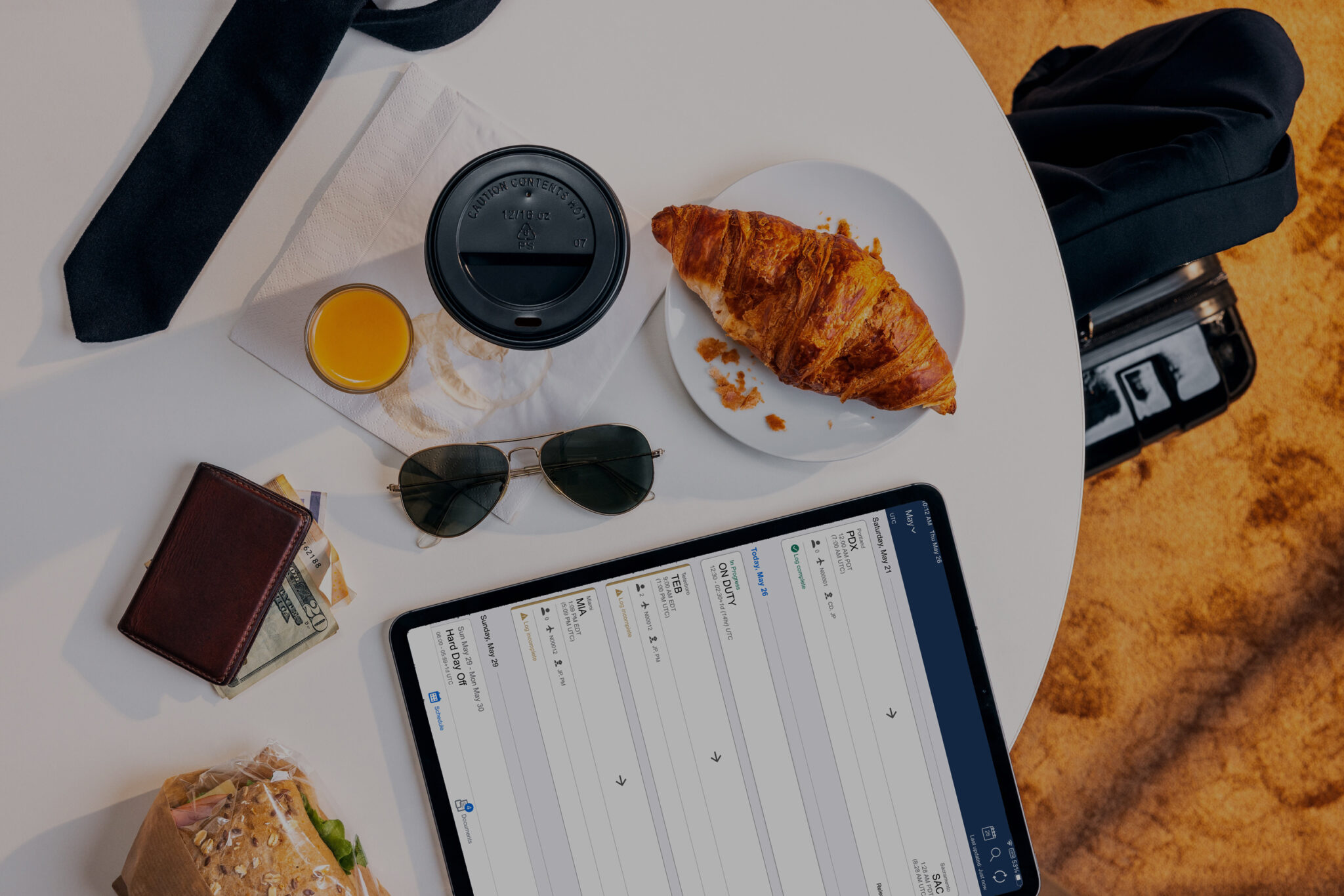 Image taken from above of the edge of a rounded white desk with an ipad, pilot glasses and food and coffee