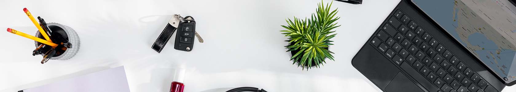 Cropped image of a white desk with a tablet, a green plant, car keys, a cup with pens