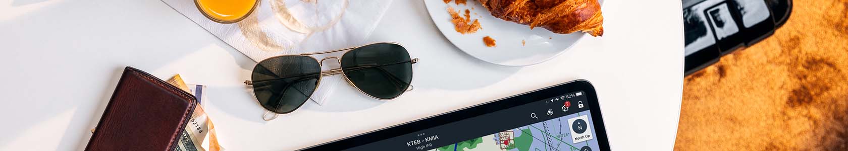 Cropped image of a rounded white table with an ipad with navigation, pilot glasses, food and coffee