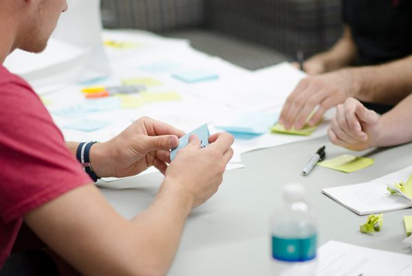 Team members collaborating on a project, using sticky notes and papers, with a water bottle on the table